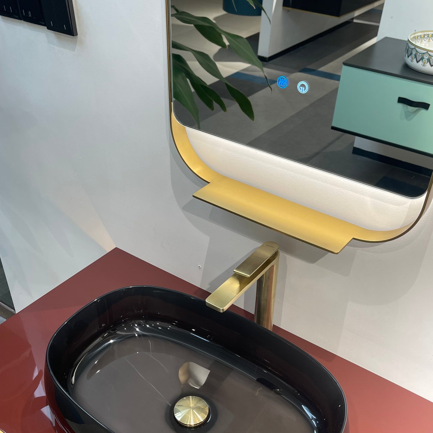 Black oval sink with gold faucet on a red countertop, mirror above